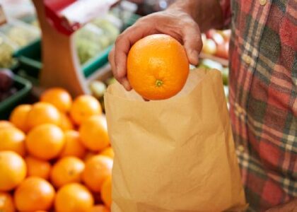 A customer at a grocery store is putting an orange in a paper bag. Did he choose the orange carefully? Or is he going through the motions?